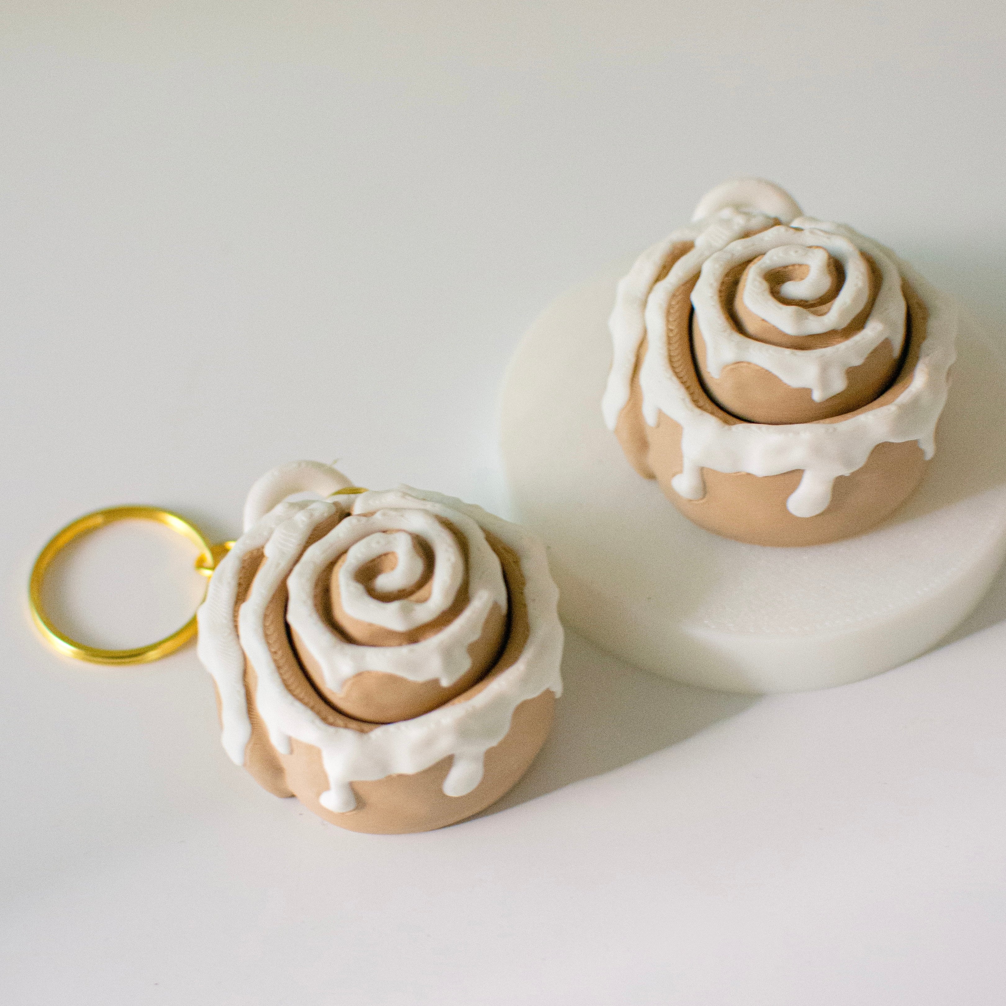 Cinnamon roll-shaped keychains with icing on a white surface.
