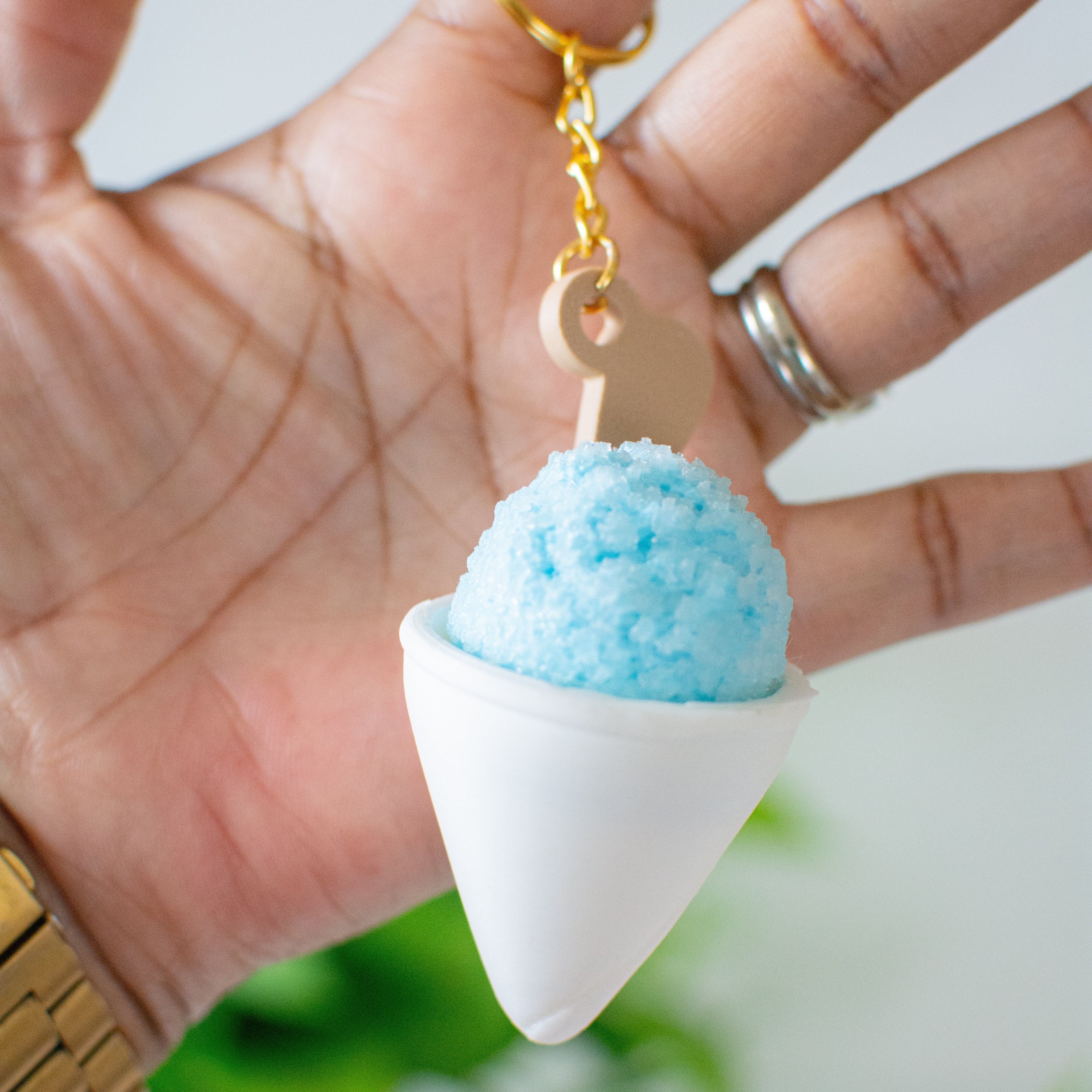 Keychain shaped like a cone with a blue top held in a hand against a blurred green background
