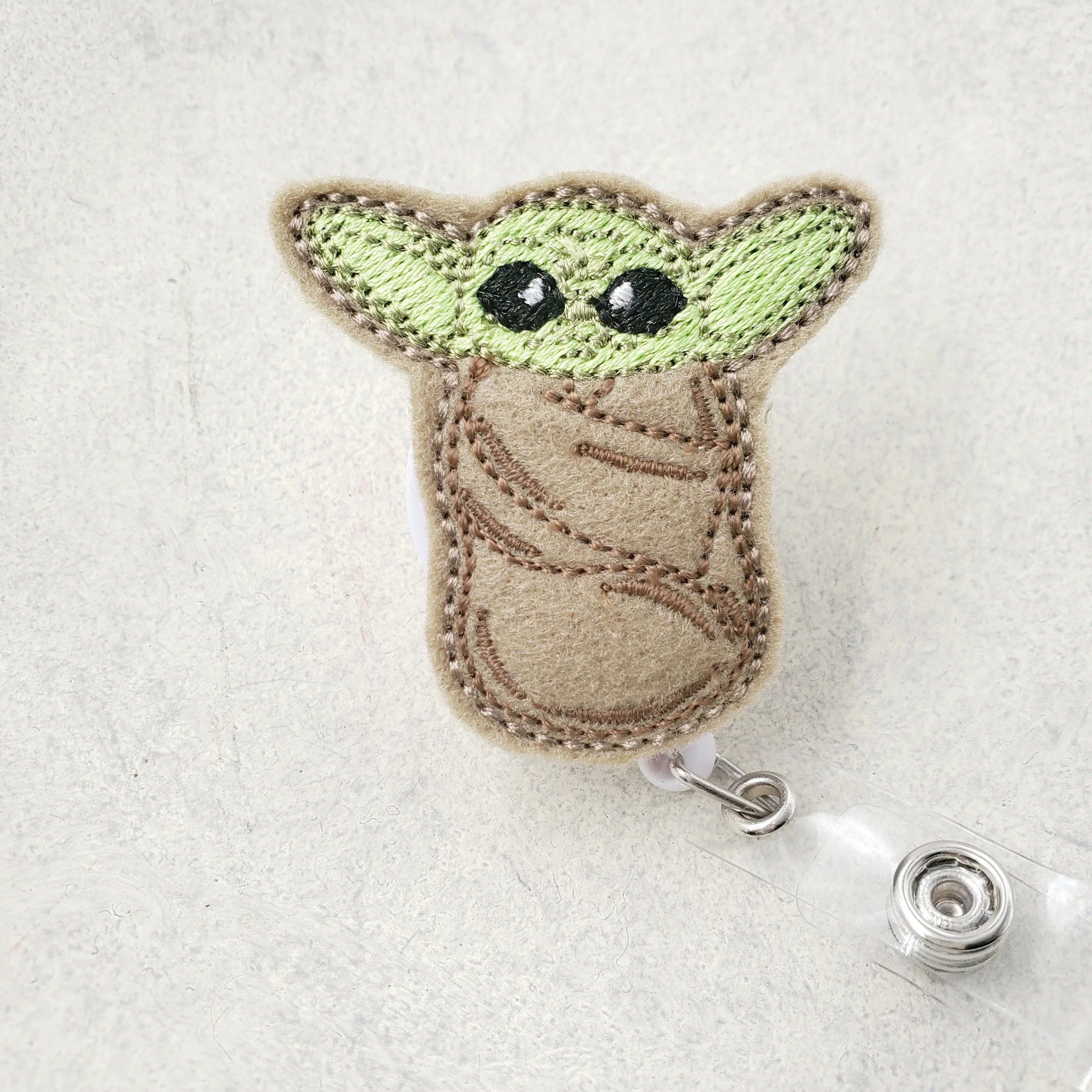 Cute embroidered baby alien badge reel with green ears and brown robe on white background