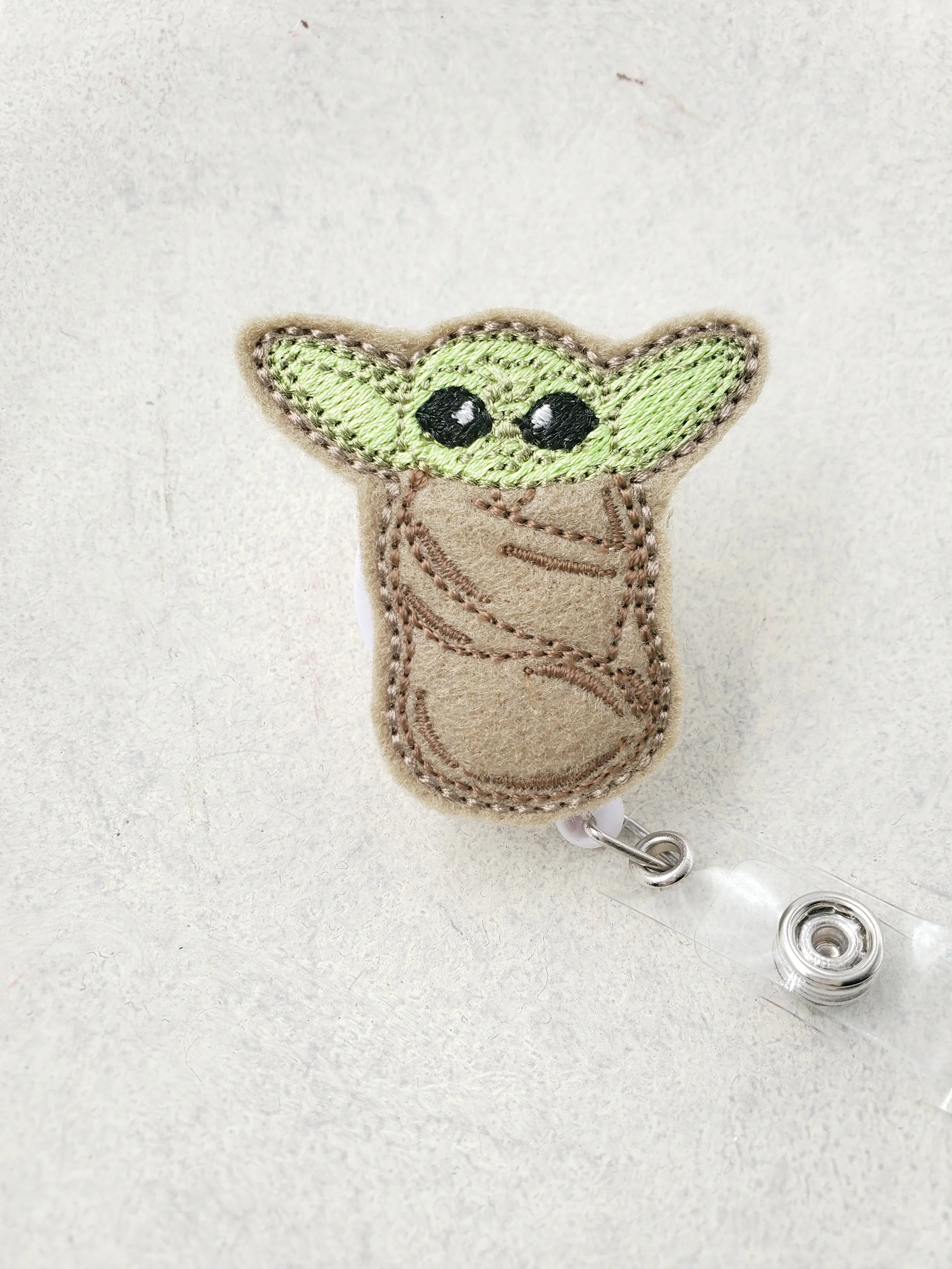 Cute embroidered baby alien badge reel with green ears and brown robe on white background