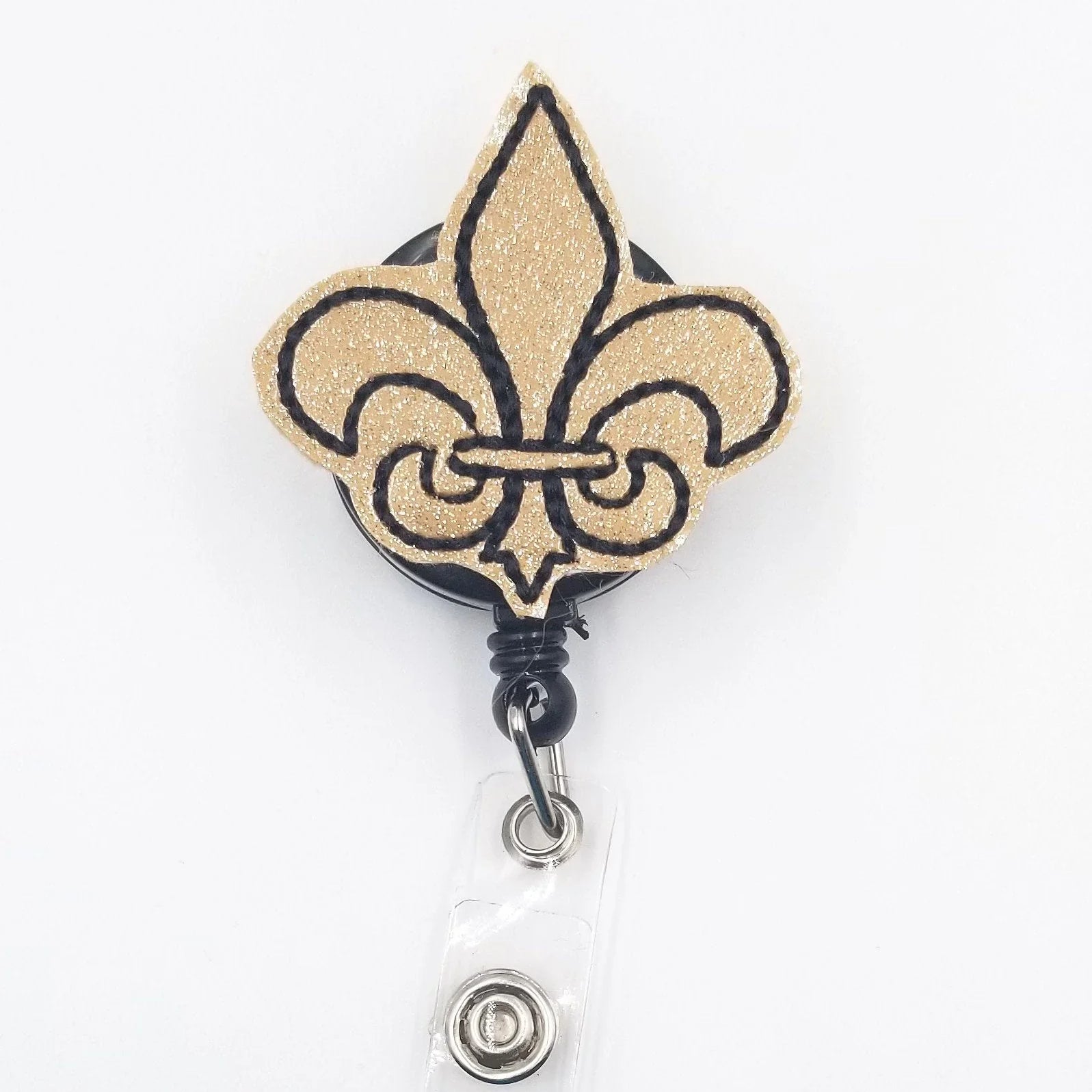 Gold glitter fleur-de-lis badge reel with black outline on white background