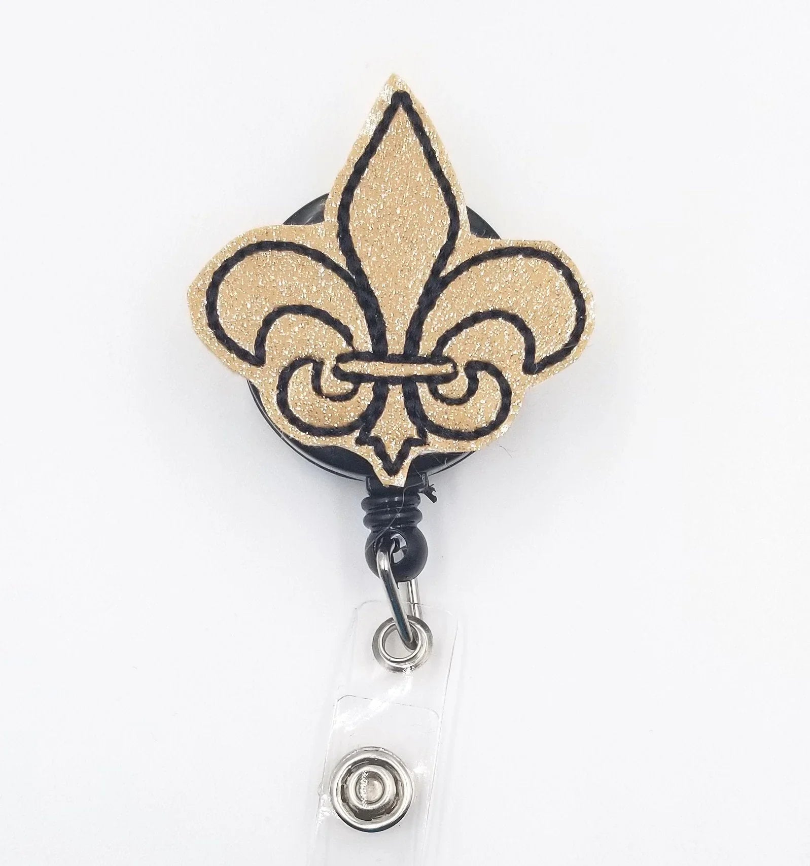 Gold glitter fleur-de-lis badge reel with black outline on white background