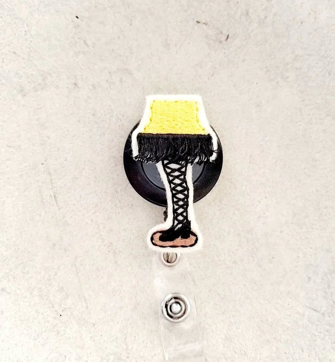 Embroidered badge reel with yellow lamp and black lace-up boot design, unique accessory
