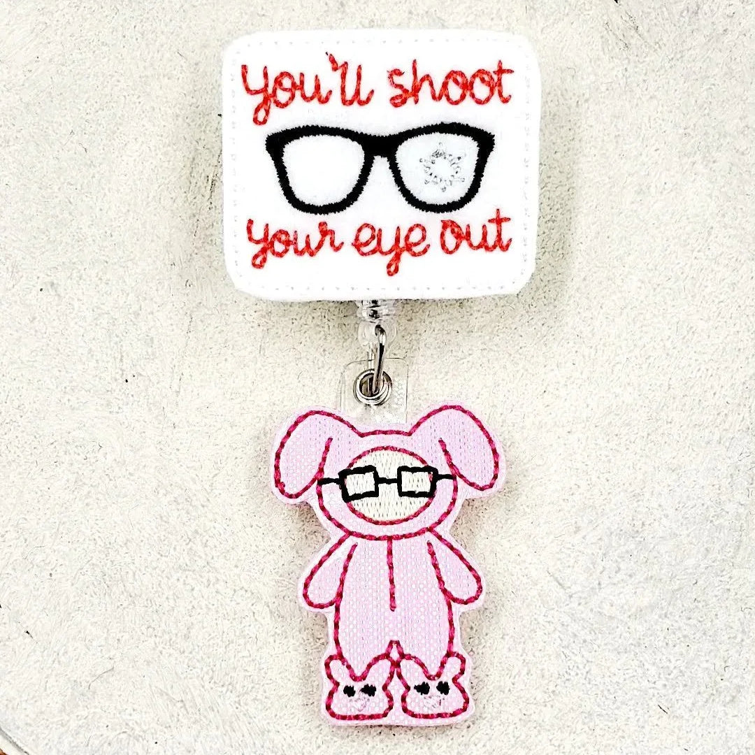 Embroidered badge reel with 'you'll shoot your eye out' text and pink bunny glasses charm.