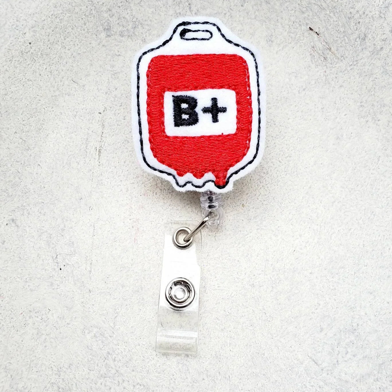 Embroidered badge reel with red blood bag and B+ symbol, nurse accessory