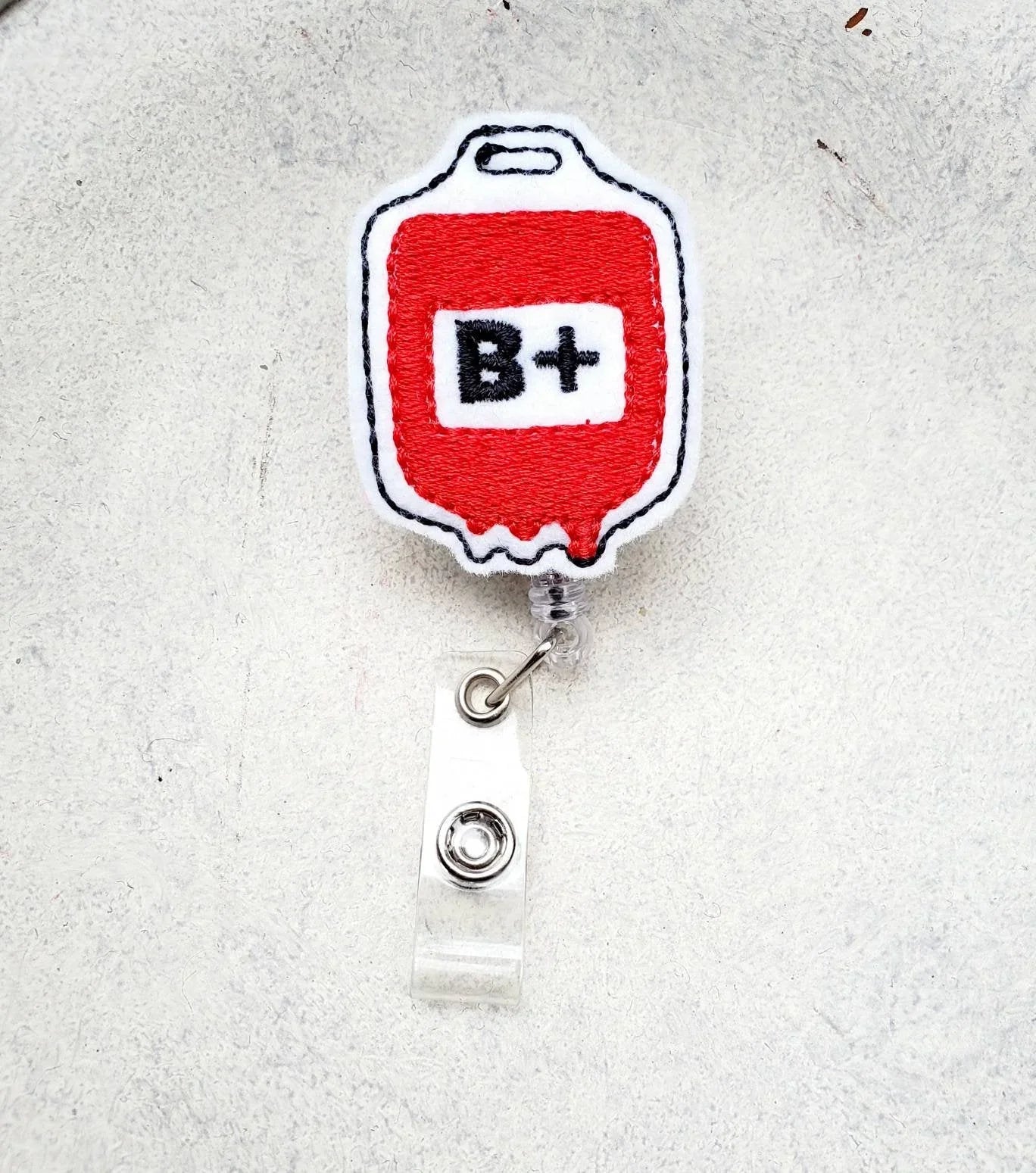 Embroidered badge reel with red blood bag and B+ symbol, nurse accessory