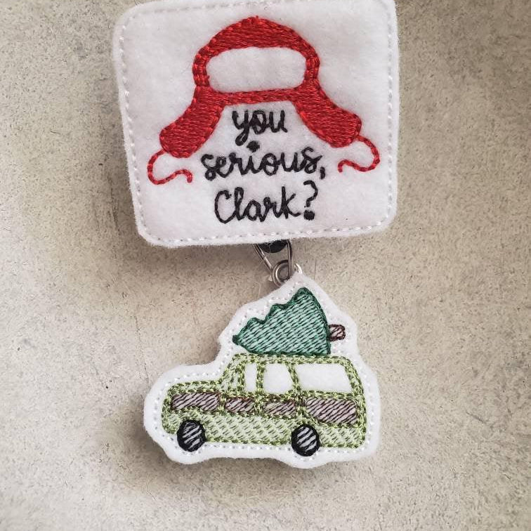 Embroidered felt badge reel with red hat, text 'you serious, Clark?' and green car with tree.