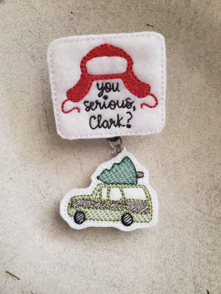 Embroidered felt badge reel with red hat, text 'you serious, Clark?' and green car with tree.