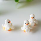 Three small white duck banana clciker fidget with orange beaks and feet on a light surface.