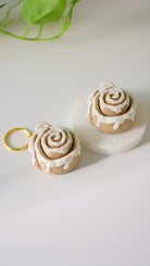 Cinnamon roll-shaped keychains with icing on a white surface.