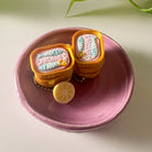 Two small can-shaped objects with 'Sardines' text on a pink plate.