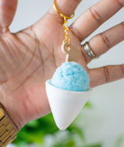 Keychain shaped like a cone with a blue top held in a hand against a blurred green background