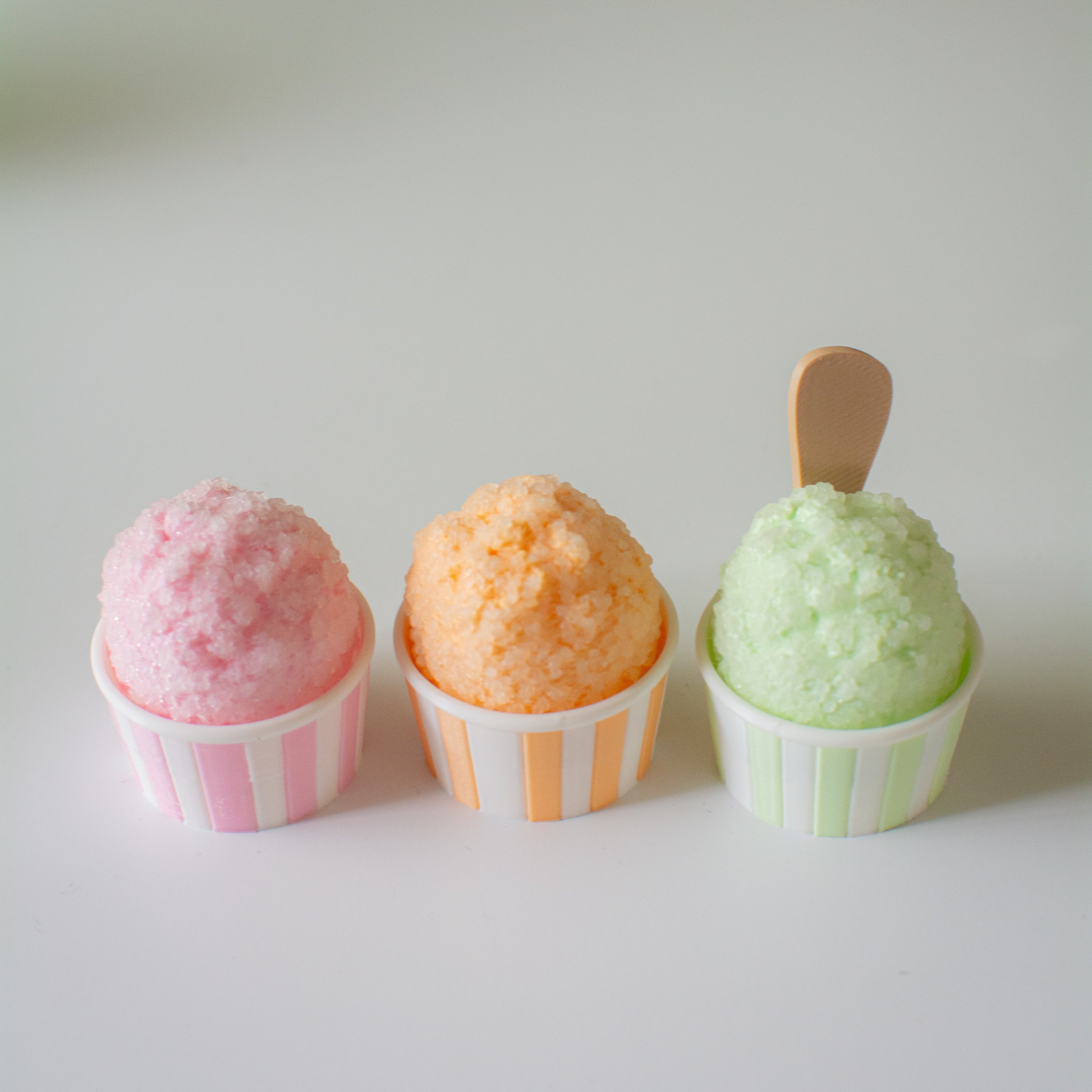 Three small snocones with pink, peach, and green ice cream on a white surface.