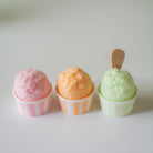 Three small snocones with pink, peach, and green ice cream on a white surface.